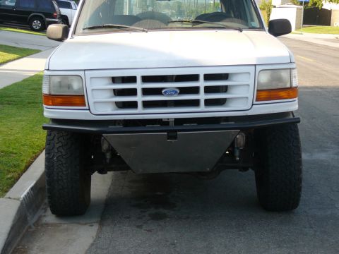 1988 Ford Bronco - The front view of a white Ford truck with an aftermarket metal bumper and large tires is parked on a residential street.