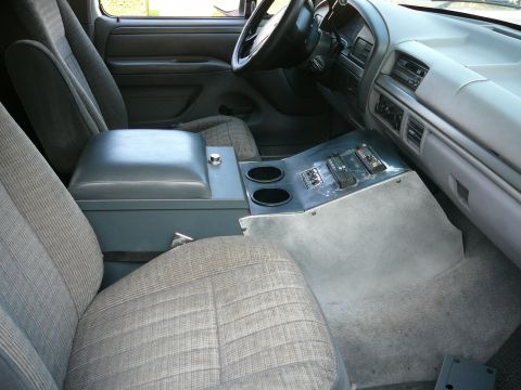 1988 Ford Bronco - The interior of a vehicle shows the driver and passenger seats, a center console with cup holders and two radios, and the dashboard with an…