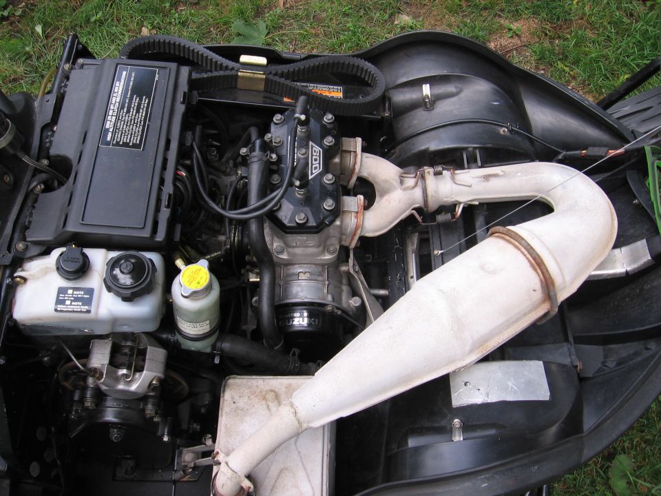 Two-stroke engine with white tuned exhaust pipe lying on grass