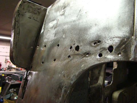 1948 Jeep Wrangler - Close-up of a bare metal body panel showing drilled holes and evidence of bodywork, likely undergoing restoration.