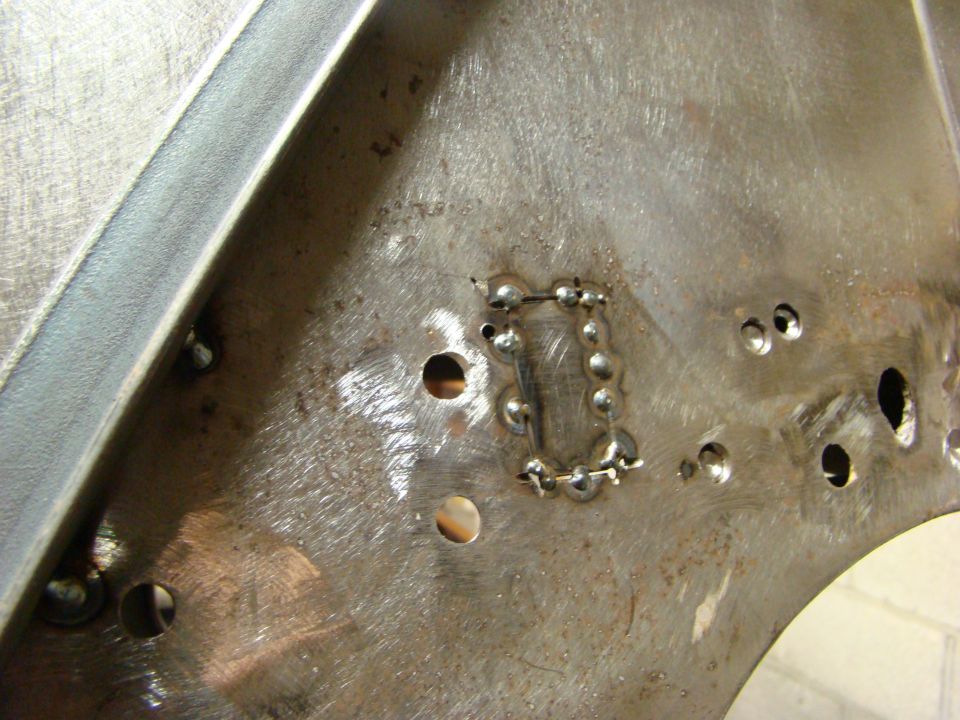 Close-up of a metal panel with several drilled holes and a rectangular patch that has been welded in place