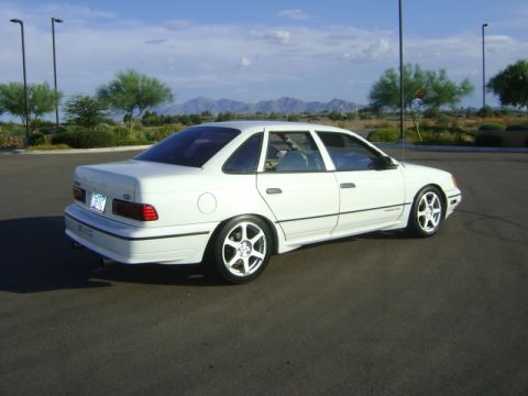 1993 Ford Taurus - A white 1993 Ford Taurus sedan is seen from a three-quarter front angle, parked outdoors with mountains in the background.