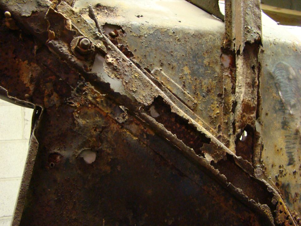 Heavily rusted metal frame with visible bolts and holes, showing significant decay