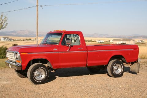 1979 Ford F-150 - A bright red 1979 Ford F-150 pickup truck is viewed from the side, parked outdoors with a rural landscape behind it.