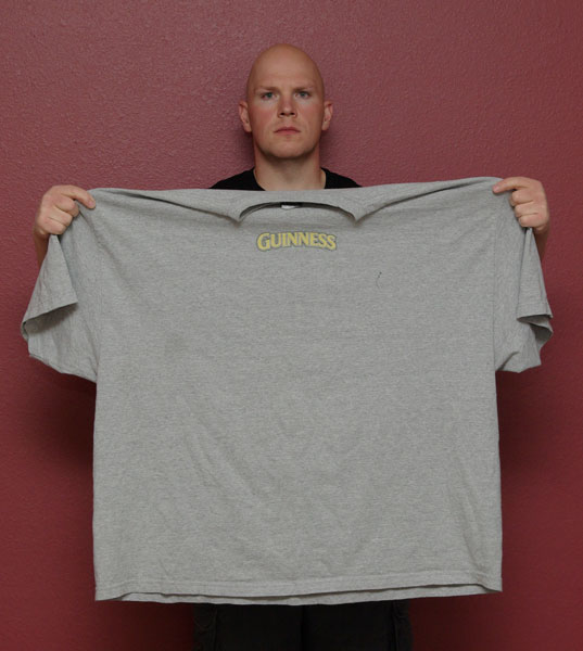 Man holding a gray Guinness T-shirt against a red wall