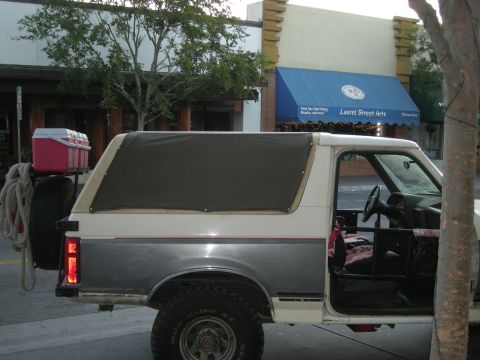 1991 Ford Bronco - A two-tone Ford Bronco is parked on a street with a storefront in the background.