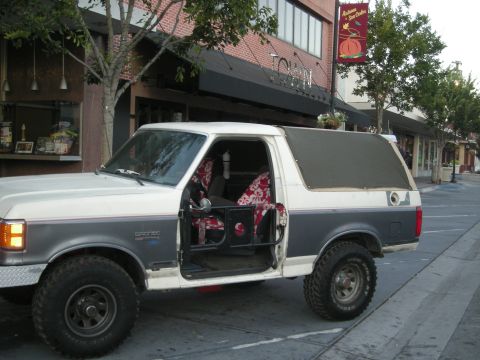 1991 Ford Bronco - A two-tone white and grey 1991 Ford Bronco is parked on a street with its driver's door open.