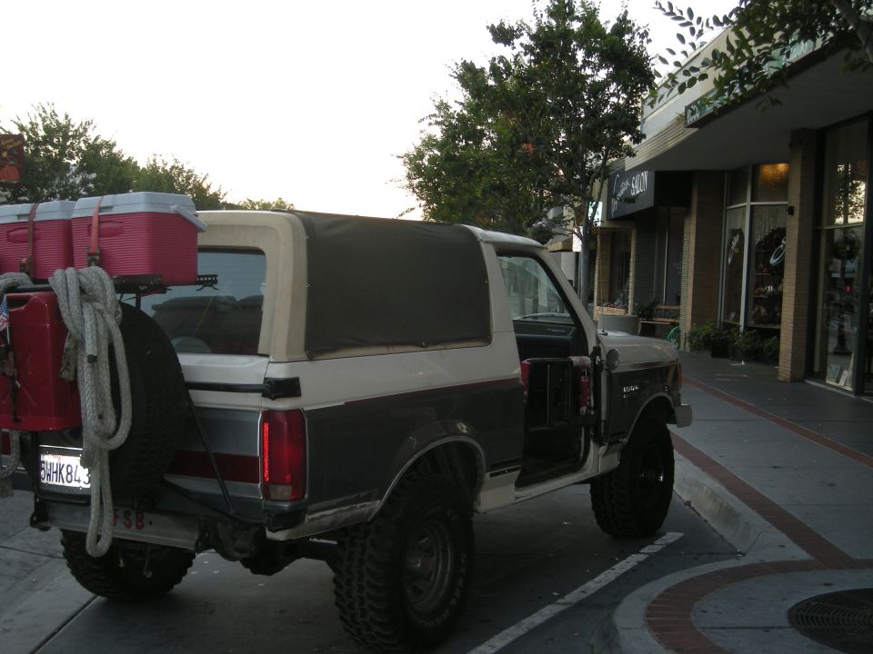 1991 Ford Bronco with soft top, spare tire mounted on rear, and two coolers on roof rack