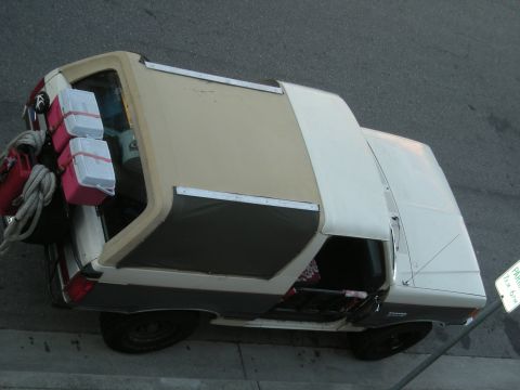 1991 Ford Bronco - A tan and white Ford Bronco is parked on the street, loaded with gear.