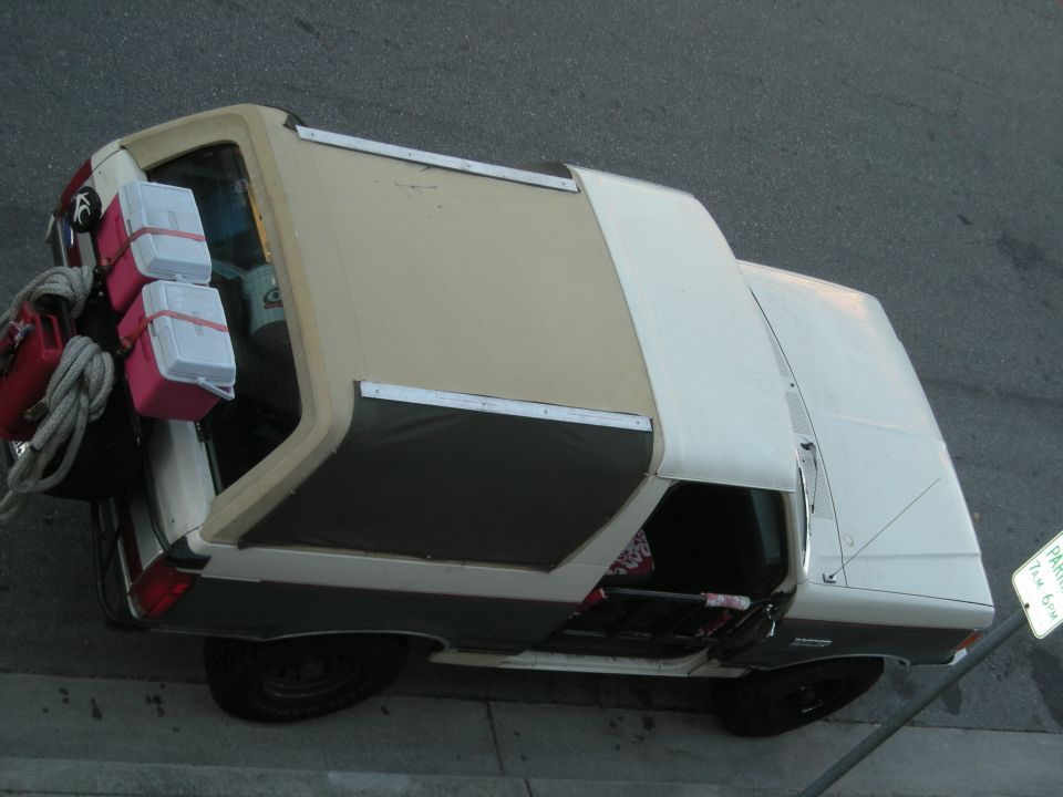 Tan and white Ford Bronco with cargo strapped to the rear, viewed from above