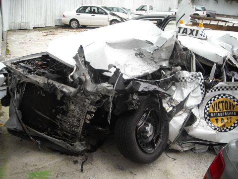 1996 Ford Crown Victoria - A severely damaged white taxi, identified as "Victory Metropolitan Taxi", sits in front of other vehicles.