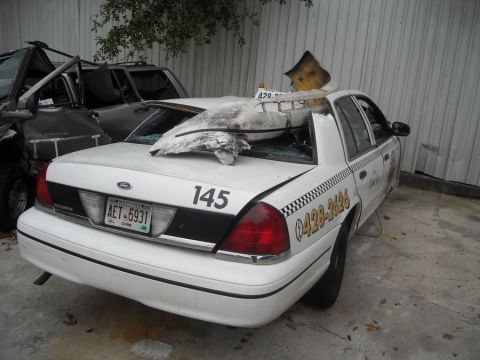 1996 Ford Crown Victoria - Damaged white taxi cab with debris on its roof, parked next to another wrecked vehicle.