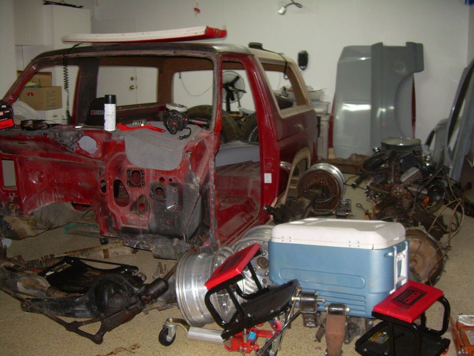 red SUV body with front end removed, parts scattered around it