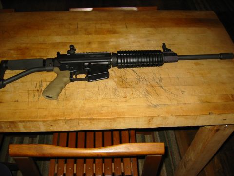 1996 Ford Bronco - An assault rifle with a tan grip and black furniture rests on a wooden surface.