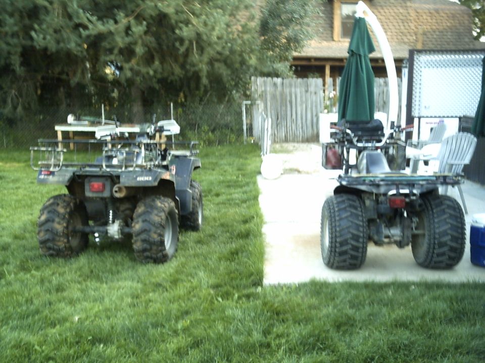 Two ATVs parked in a backyard, one in grass at left and one on a concrete patio at right.