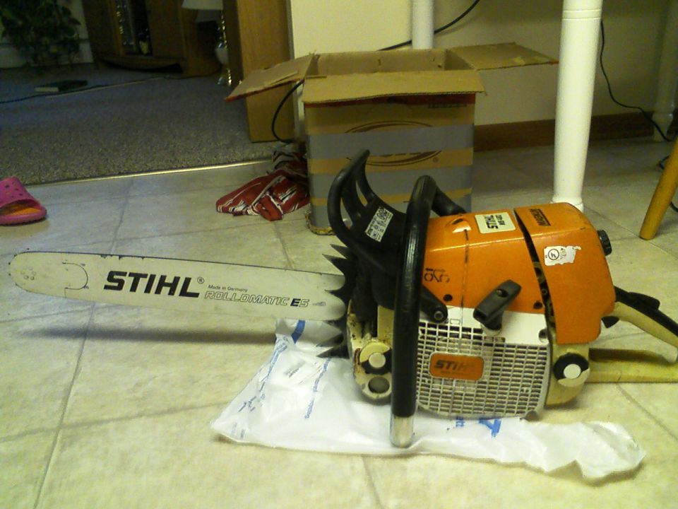 Stihl chainsaw with long guide bar and box on tile floor