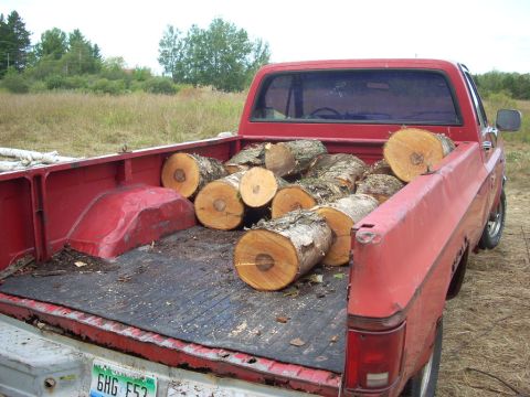 2000 Chevrolet Tahoe - A red pickup truck is loaded with cut logs, ready for transport or use.