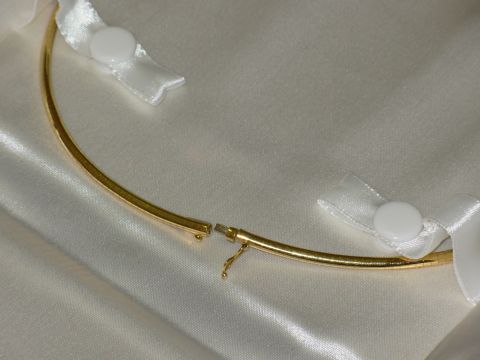 2004 Land Rover Land Rover - A gold necklace is displayed on a white satin background, secured with white ribbons.