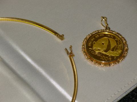 2004 Land Rover Land Rover - A gold panda coin pendant is shown next to an open necklace clasp on a white satin surface.