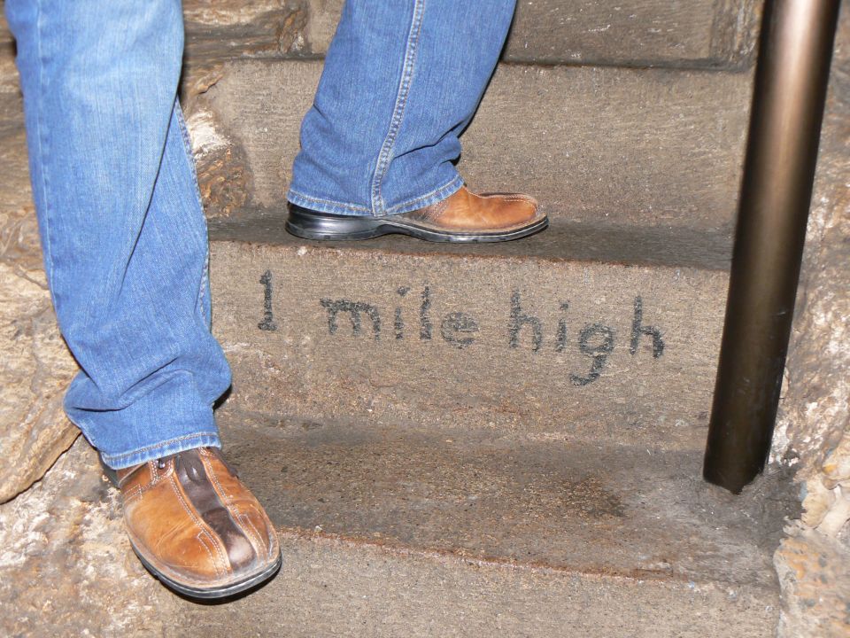 Stone steps with text '1 mile high' and people's legs in jeans and brown shoes
