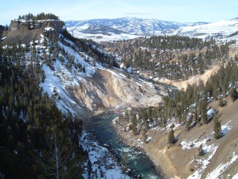 2006 Ford E350 - A wide river cuts through a snow-dusted canyon landscape, bordered by pine trees and distant mountains.