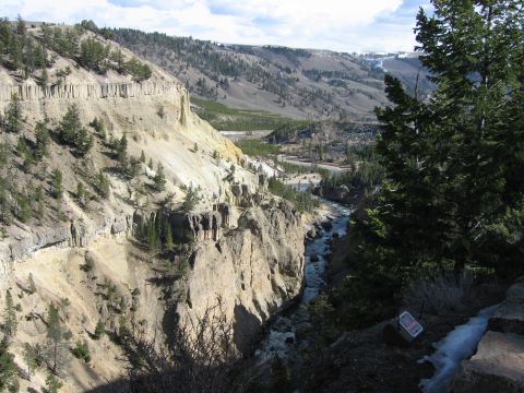 2006 Ford E350 - A wide canyon carved by a river, with steep, textured cliffs and distant mountains under a partly cloudy sky.