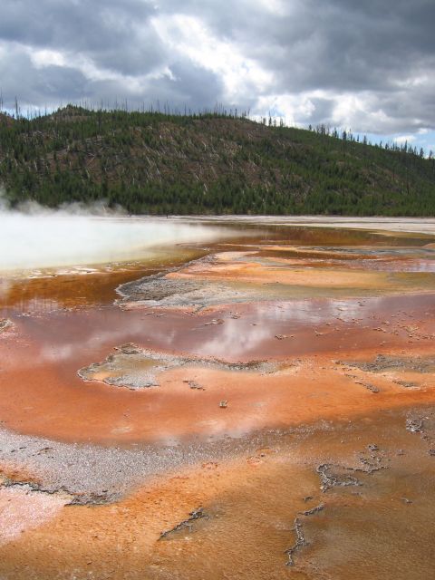 2006 Ford E350 - A natural landscape a steaming geothermal pool with vibrant mineral deposits and a distant tree-covered hill.