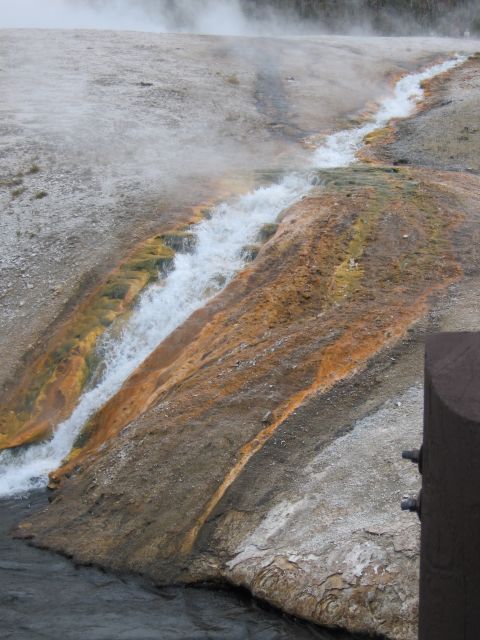 2006 Ford E350 - A natural hot spring flows over mineral-rich rocks, creating vibrant orange and yellow hues amidst rising steam.