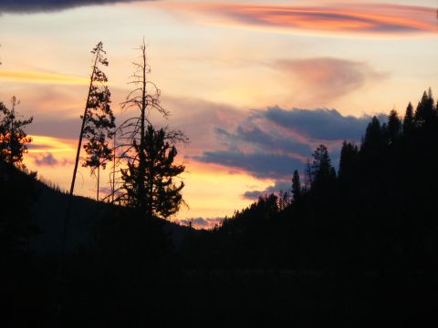 2006 Ford E350 - A vibrant sunset paints the sky with hues of orange, pink, and purple above a dark, forested mountain landscape.