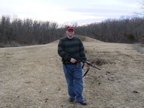 2006 Ford E350 - A man stands in a field holding a rifle, with spent shell casings scattered on the ground.