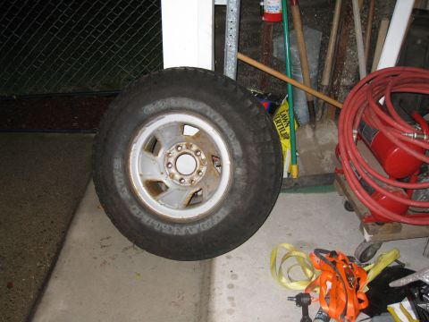 1996 Ford Bronco - A single tire and wheel assembly is shown, with various tools and equipment visible behind it.