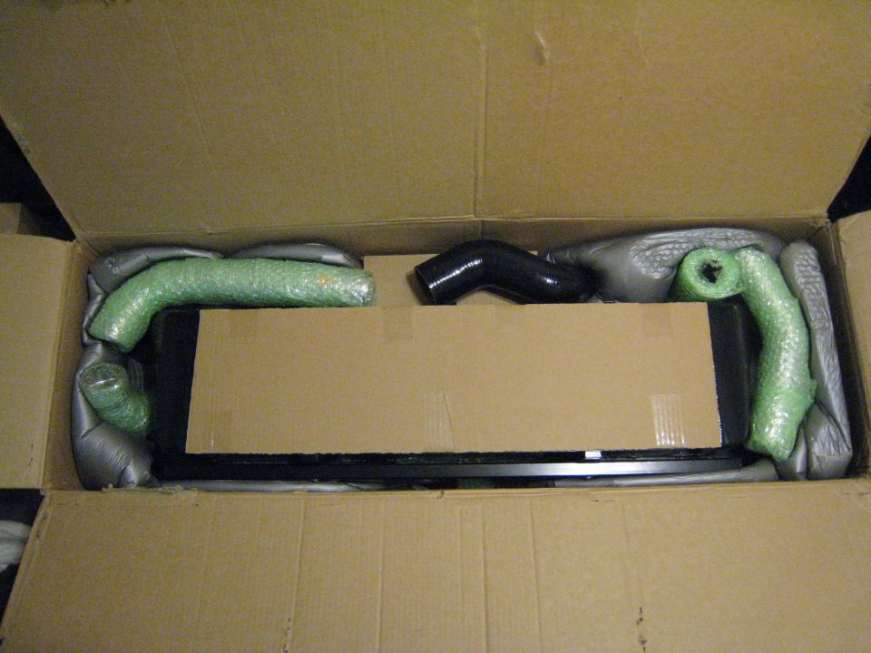 New black front-mount intercooler and charge pipes packed in a cardboard shipping box