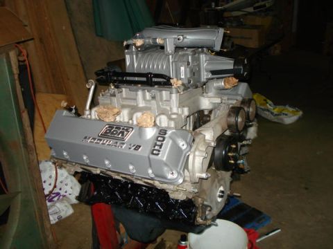 2007 Ford Mustang - A silver modular V8 engine with a supercharger is displayed on a stand in a garage setting.