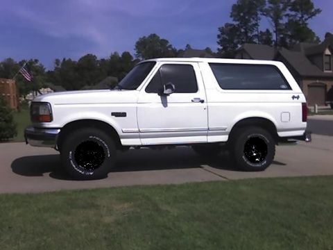 1987 Ford Bronco - A white SUV is parked in front of a house on a sunny day.