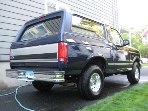 1995 Ford Bronco - The rear-right quarter view of a dark blue Ford Bronco shows its chrome bumper and silver trim details.