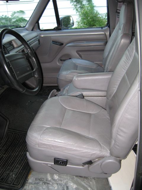 1995 Ford Bronco - The interior of a vehicle shows gray leather seats, armrests, and part of the dashboard.