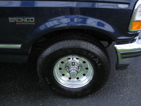 1995 Ford Bronco - Close-up of the front wheel and fender of a dark blue 1995 Ford Bronco XLT.