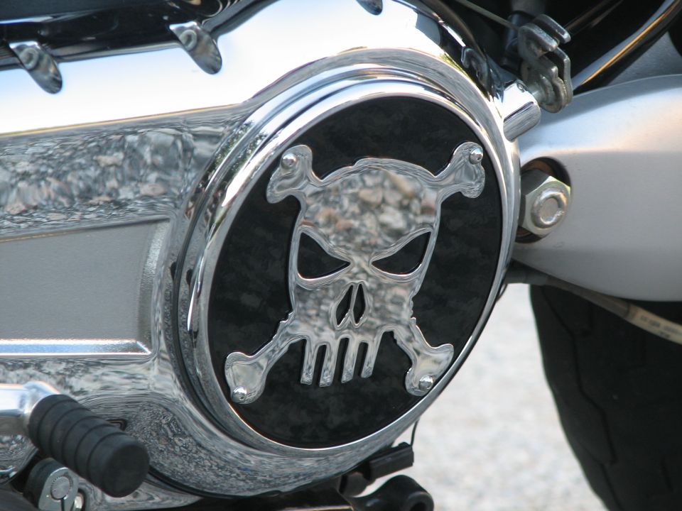 Close-up of a motorcycle engine cover with a chrome skull and crossbones emblem on a black background