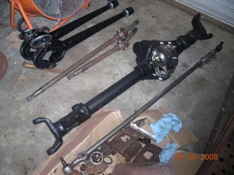 1993 Ford Bronco - Various vehicle axle and steering components are laid out on the floor, some in boxes.