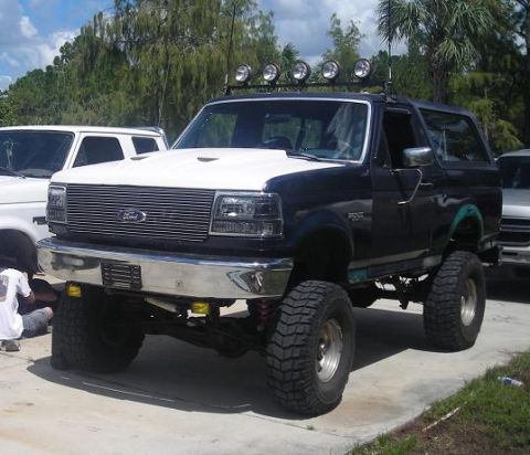 1993 Ford Bronco - A lifted Ford Bronco with a two-tone paint job is parked outdoors next to another white vehicle.
