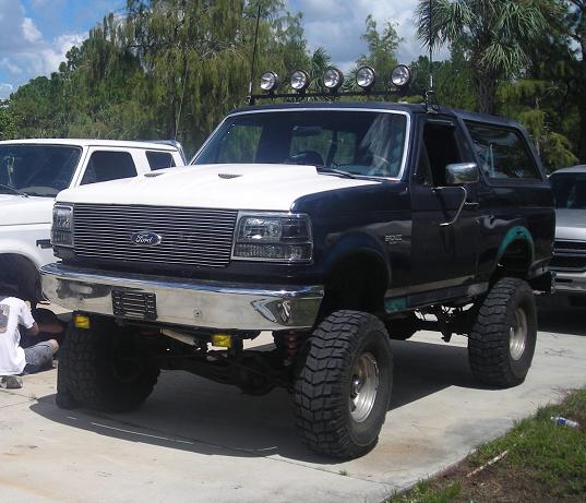 Black and white Ford Bronco with off-road tires and light bar, parked on concrete