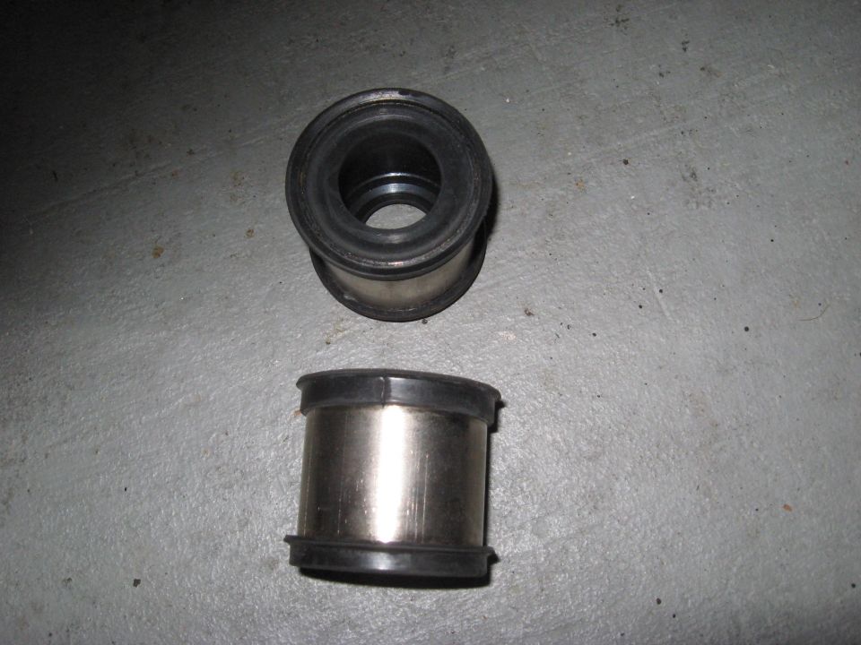 Two metal and rubber bushings on a gray concrete surface