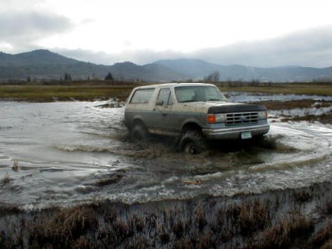 1988 Ford Bronco - Ford Bronco navigating a flooded area with a mountainous landscape behind it.