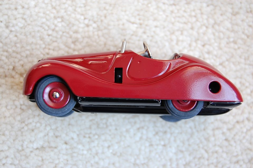 Red tinplate toy roadster with twin aero screens shot from above on cream carpet