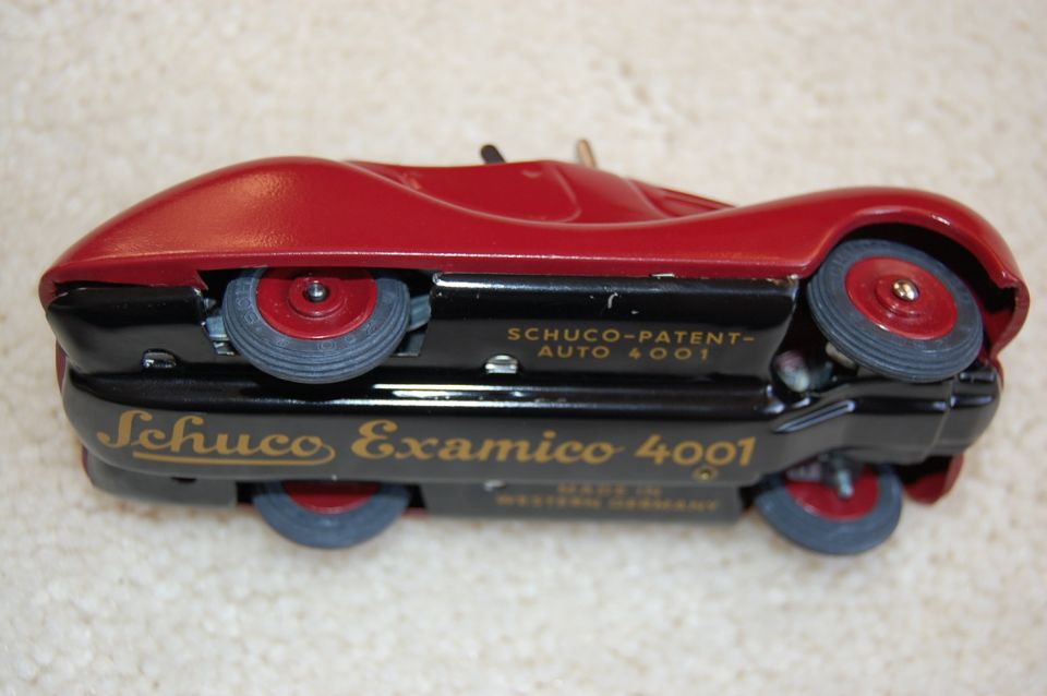 Red Schuco Examico 4001 tin toy car upside down on carpet showing gold-lettered black chassis