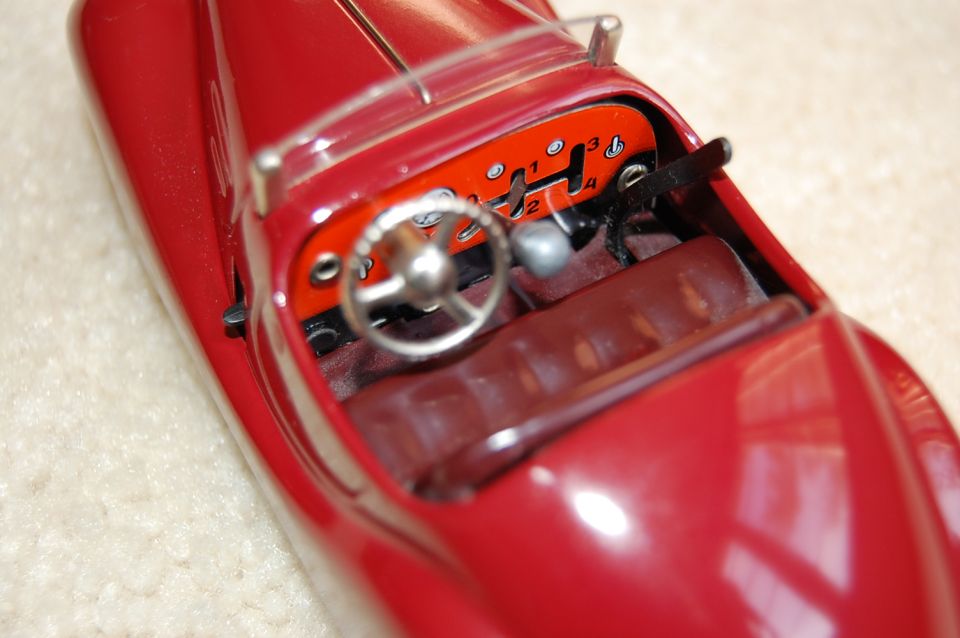 Close-up of red tin toy car cockpit with chrome steering wheel and numbered orange shift gate