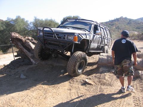 1989 Ford Bronco - This modified Toyota V6 SUV is shown tackling a challenging off-road obstacle with a person observing nearby.