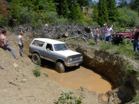 1988 Ford Bronco - A 1988 Ford Bronco tackles a challenging mud obstacle while onlookers observe the off-road action.