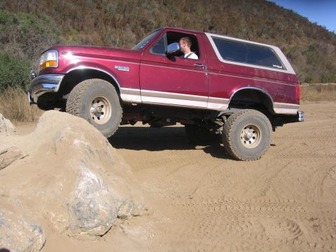 1989 Ford Bronco - A red Ford Bronco navigates rocky terrain on a sunny day.