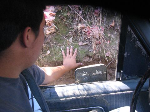 1989 Ford Bronco - A person peers out the window of a vehicle stuck in mud, with vegetation visible on the embankment.